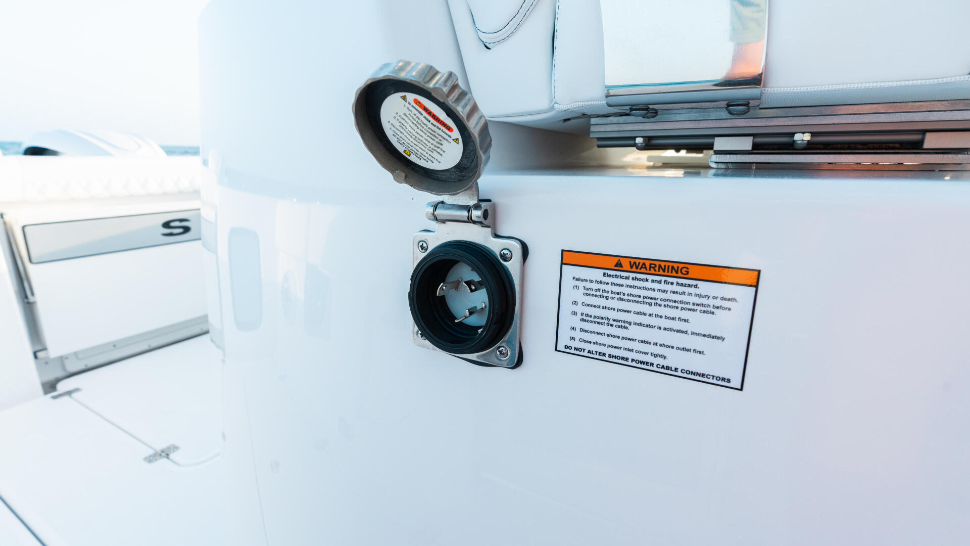 Electrical shore power outlet and warning label mounted on the white exterior of a boat