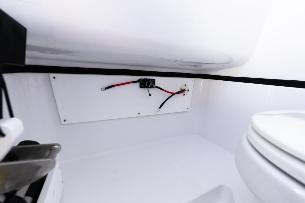 Electrical panel with black switch and red wiring installed inside boat cabin storage area