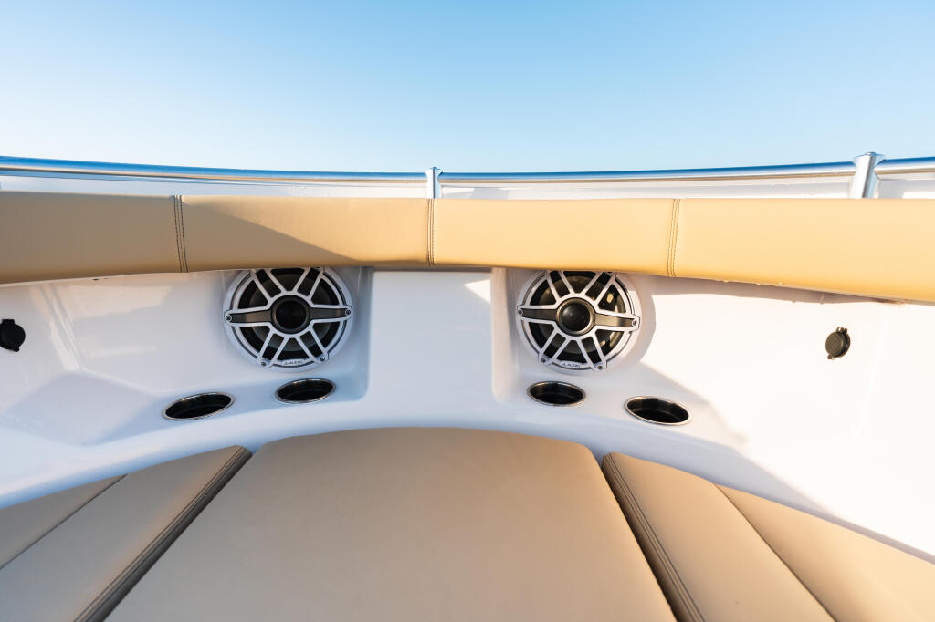 Boat interior showing tan upholstered seating, dual marine speakers, and blue canvas bimini top against clear sky