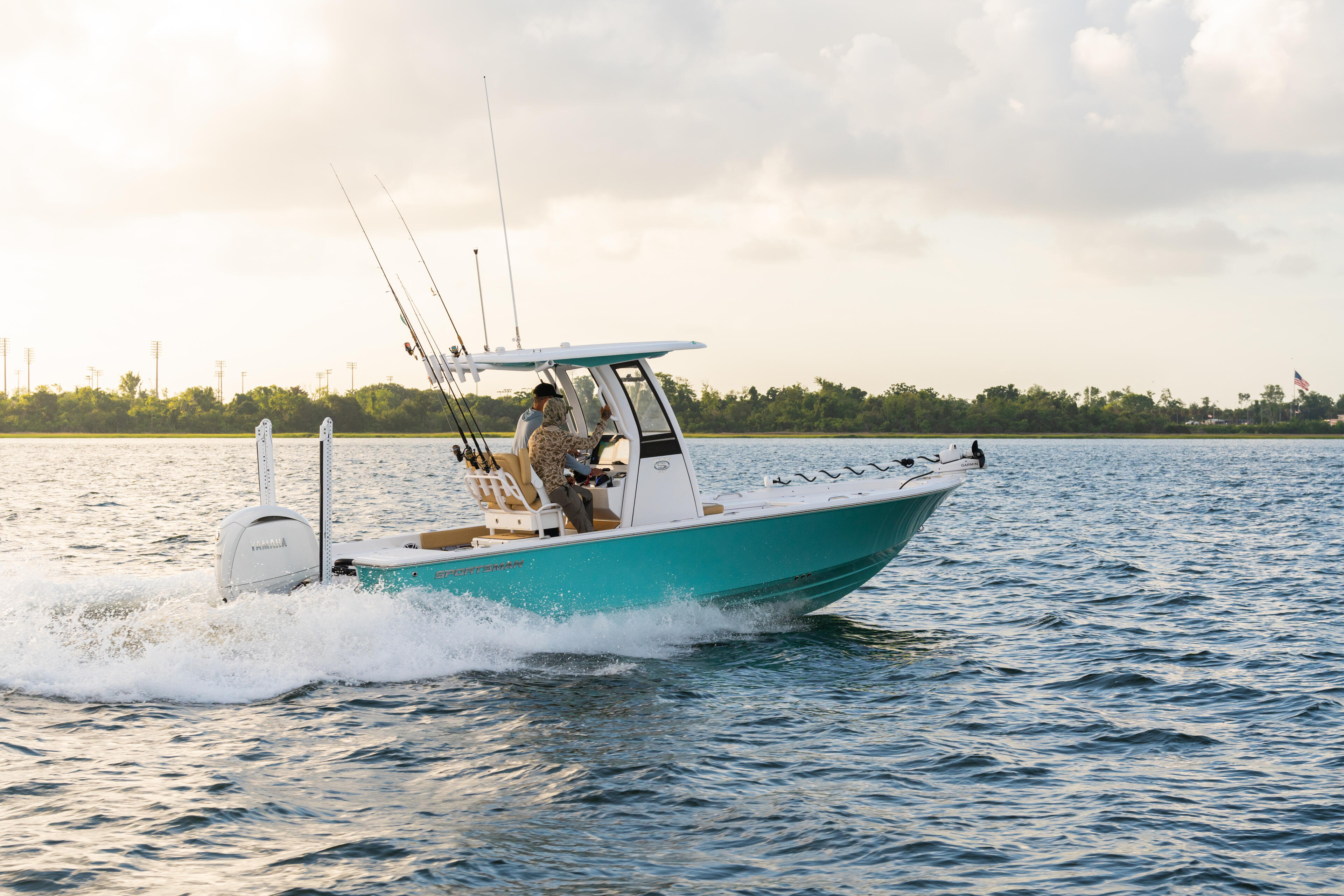 Turquoise fishing boat with multiple rods running through shallow water near shore