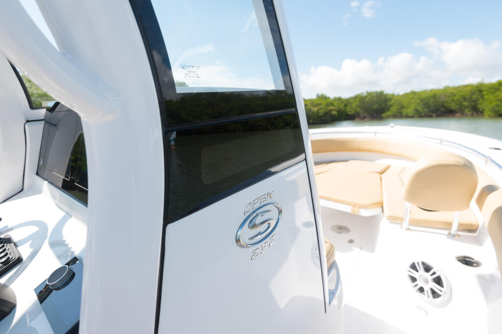 Open center console boat with tinted windows and cream-colored seating, docked near mangrove shoreline