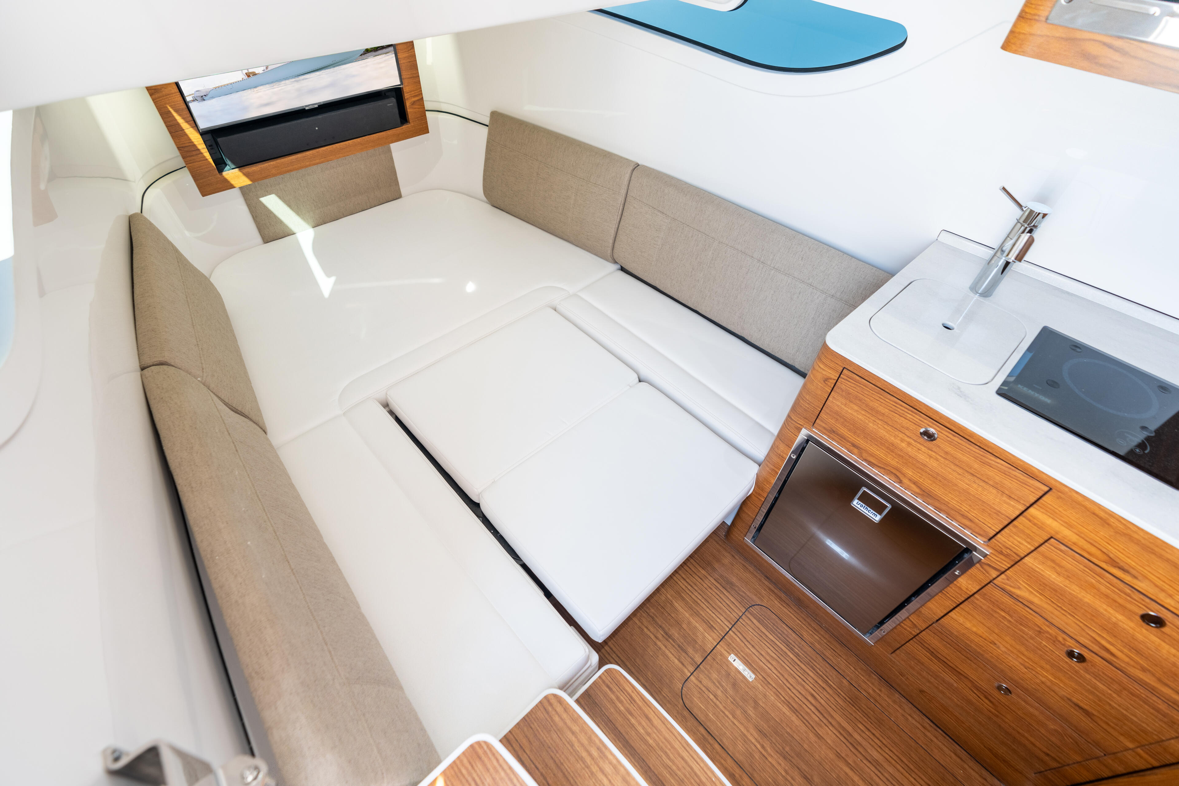 Spacious cabin interior with beige upholstered seating, white berths, wood cabinetry, and galley counter with sink