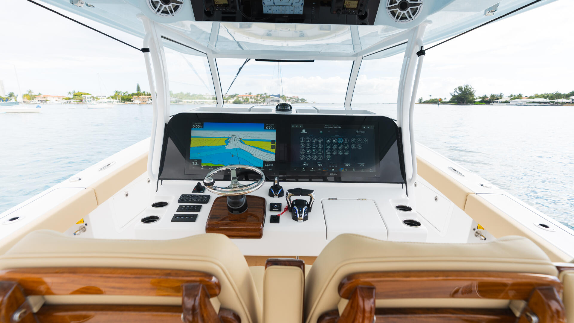 Helm station with dual displays, steering wheel, and overhead speakers under a hard-top canopy overlooking calm waters