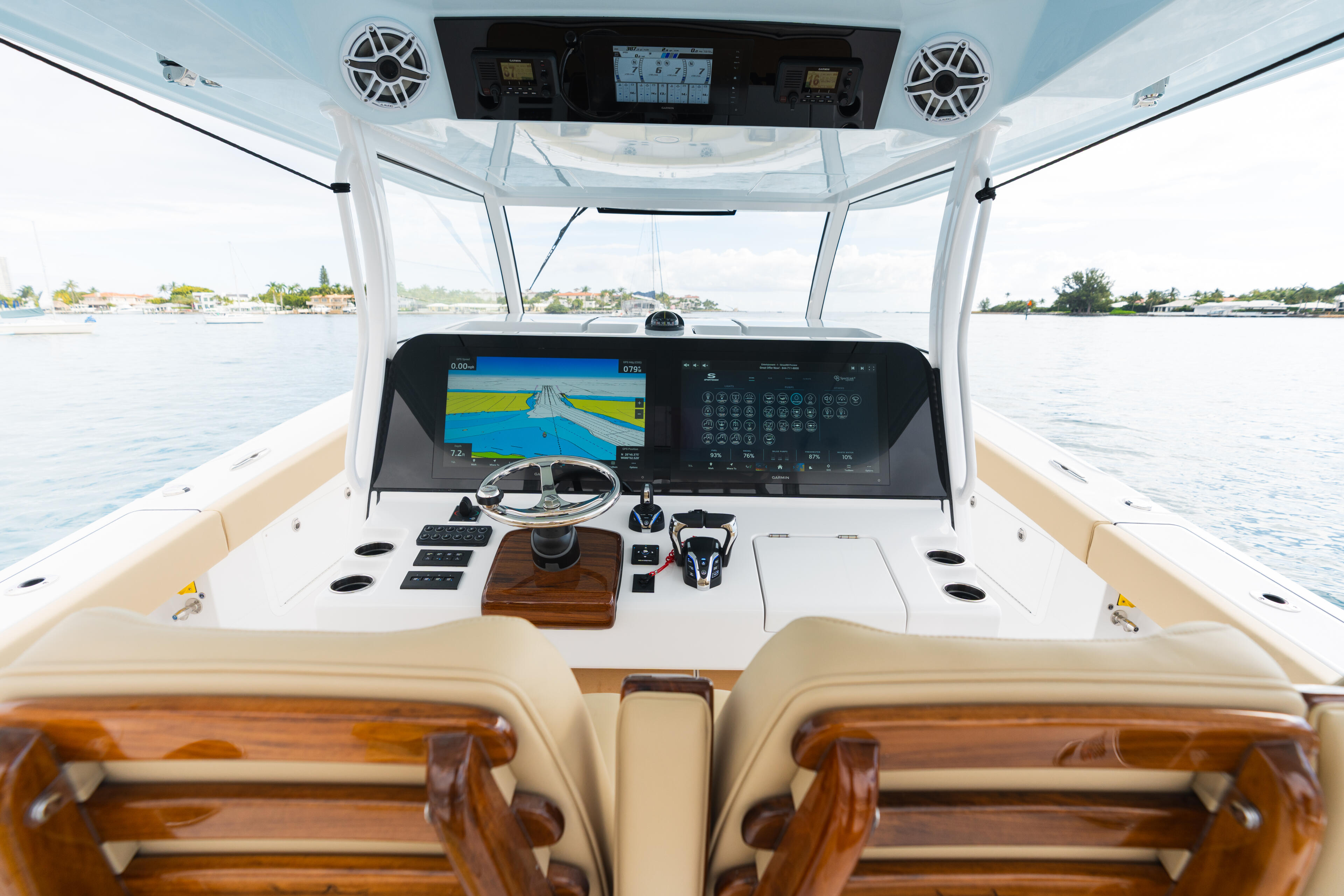 Helm station with dual displays, steering wheel, and overhead speakers under a hard-top canopy overlooking calm waters