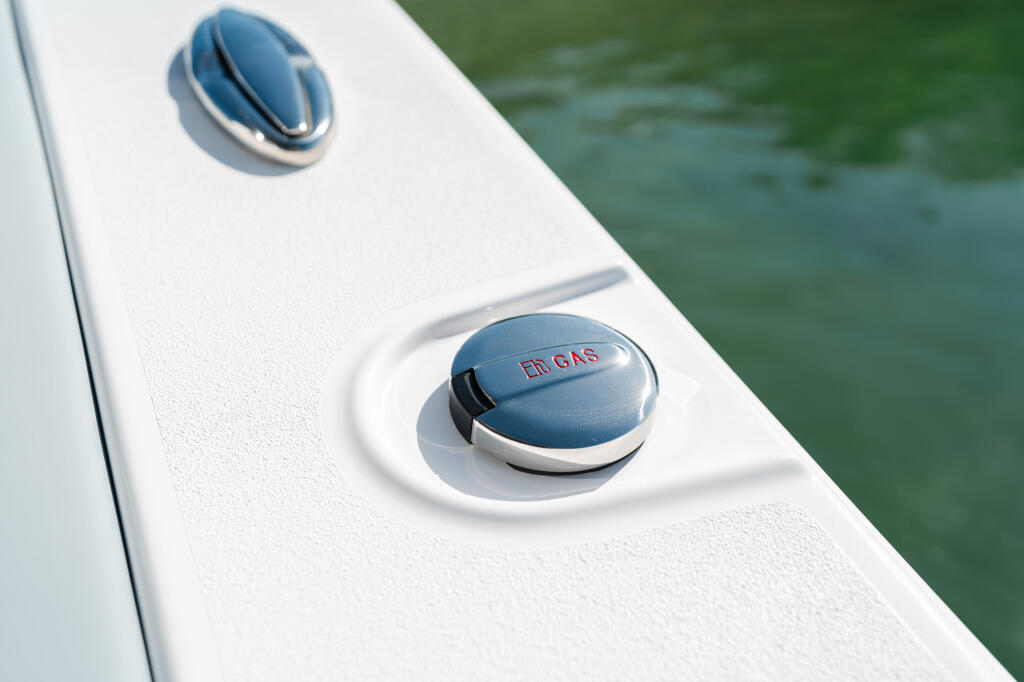 Blue and silver boat fuel cap and vent on white gunwale above green water