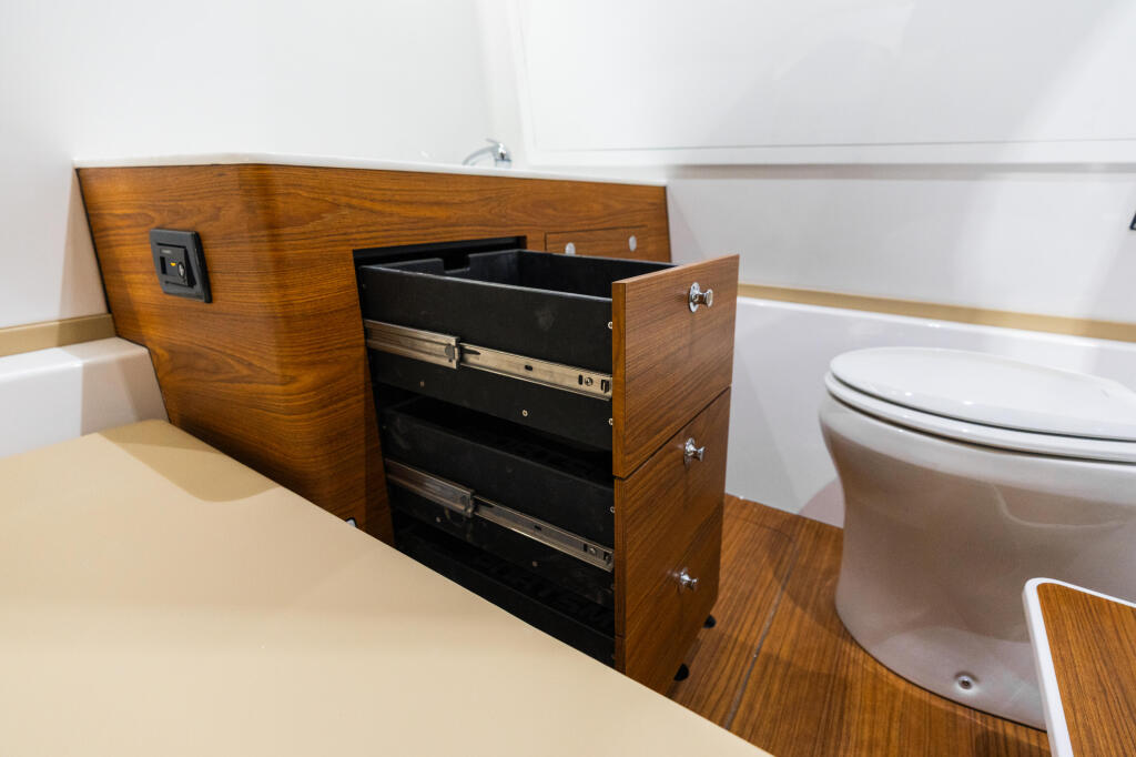 Boat cabin bathroom with wooden cabinetry, pull-out storage drawer, and white porcelain toilet