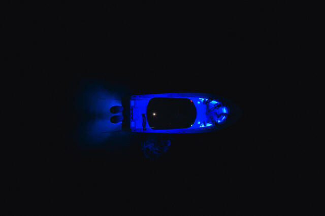 Boat viewed from above at night with bright blue underwater lighting illuminating the hull