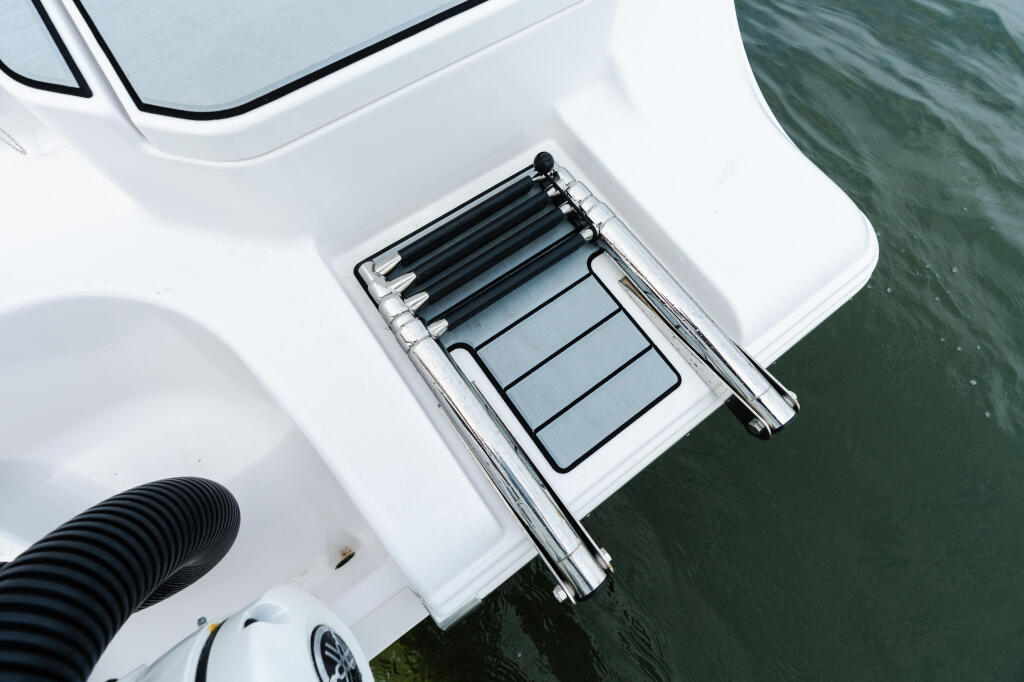 Overhead view of a boat's white gunwale with black fishing rod holders and gray storage compartments docked in water