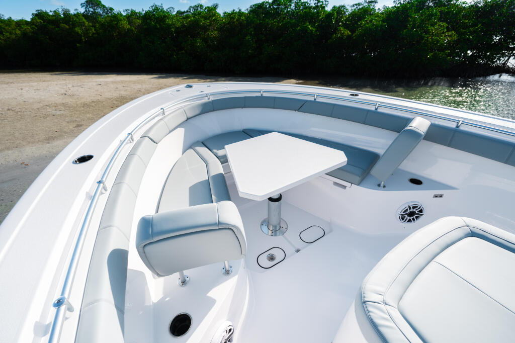 Overhead view of boat cockpit with white upholstered seating, helm controls, and mangrove shoreline in background