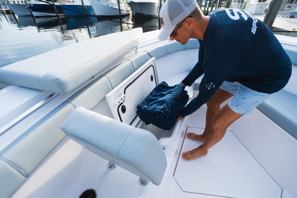 Man accessing boat storage compartment at marina dock with other boats moored in background