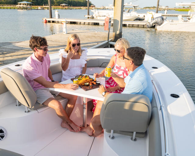 Four friends enjoying appetizers and drinks on a boat docked at a marina