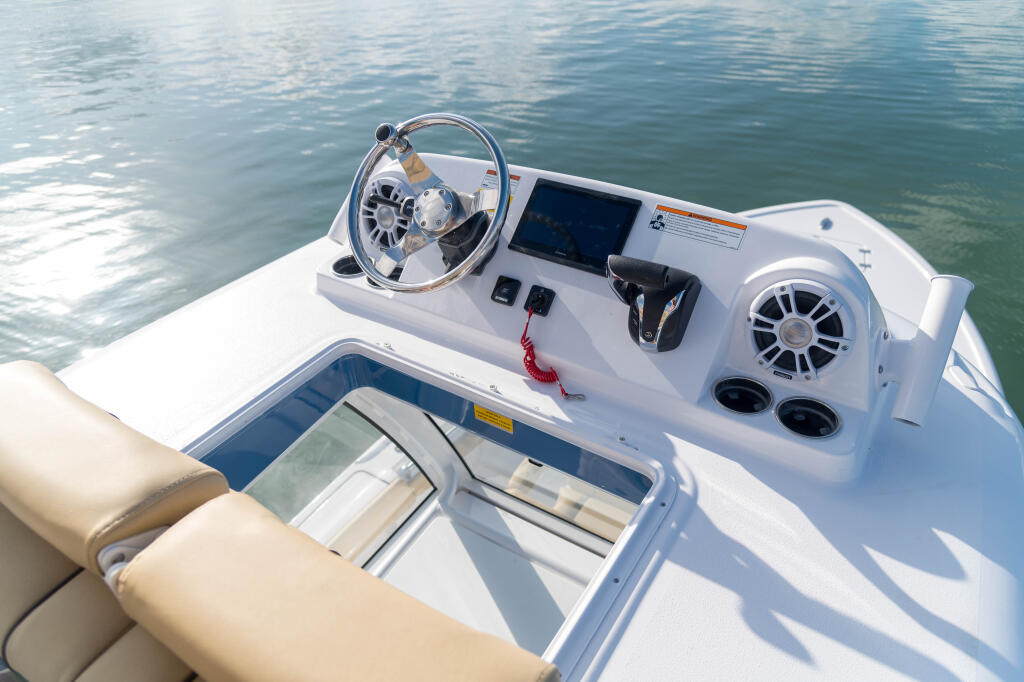 Helm station with steering wheel, dual monitors, controls, and audio speakers on a white center console boat