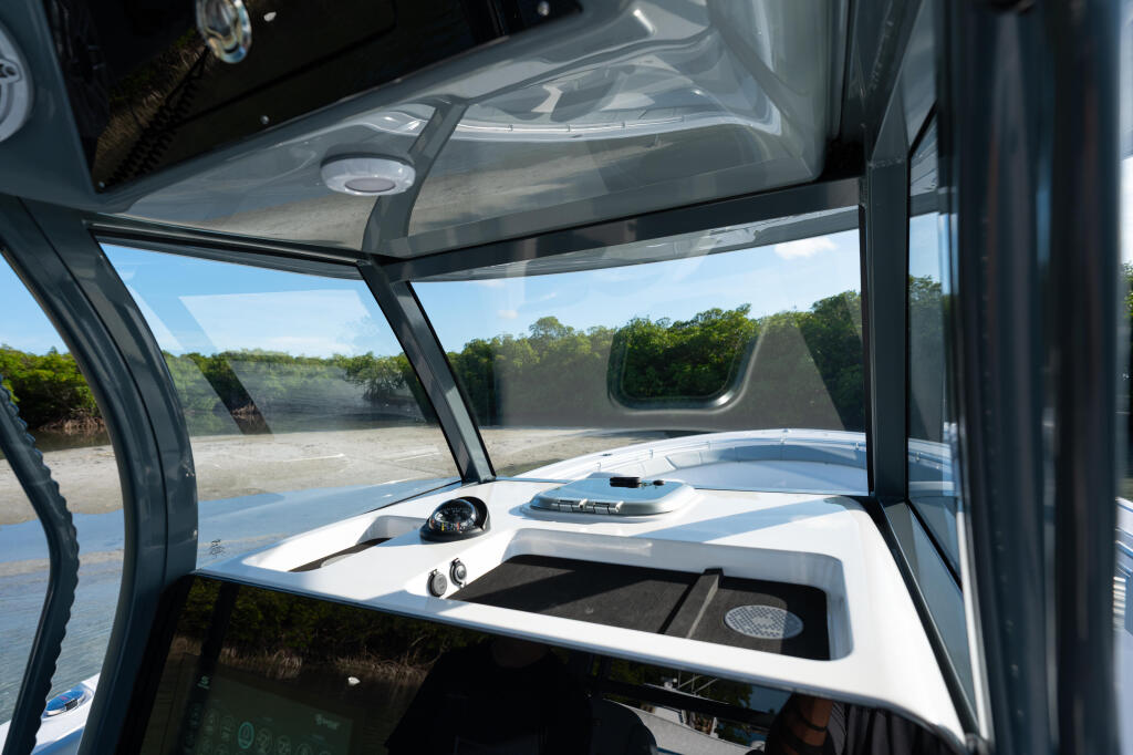 Hard-top cabin view showing helm station with windshield overlooking shallow mangrove waterway