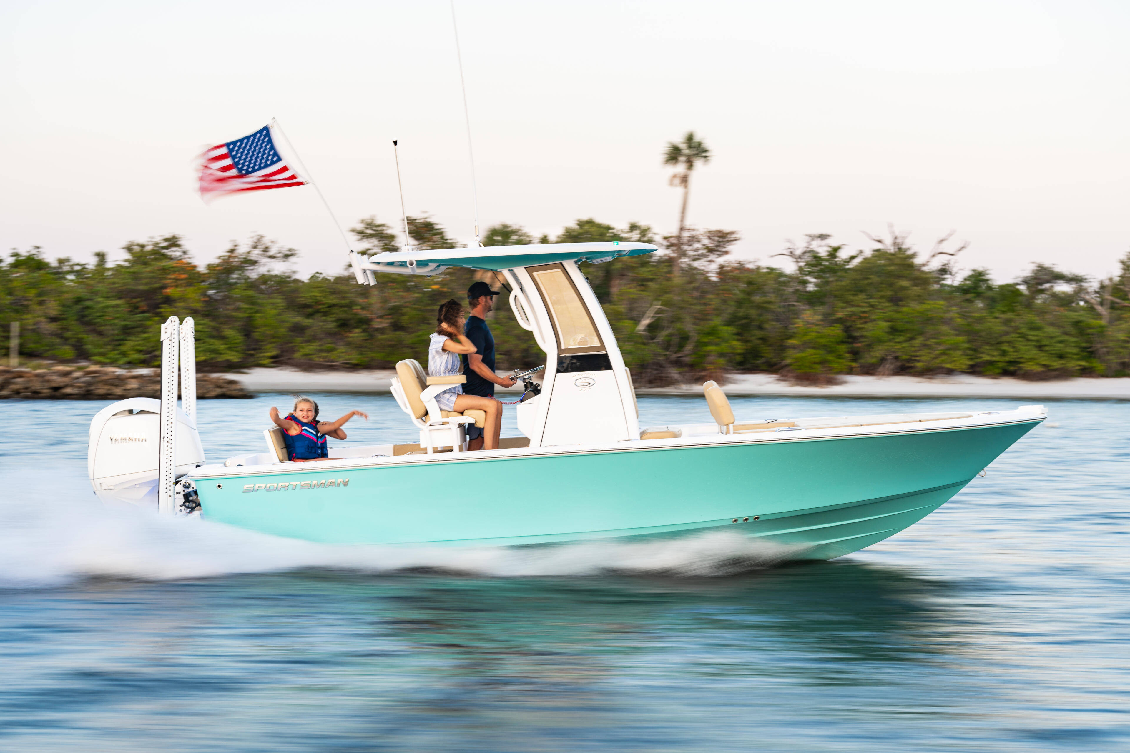 Turquoise center console boat running in shallow water with family and young child, American flag flying from hardtop