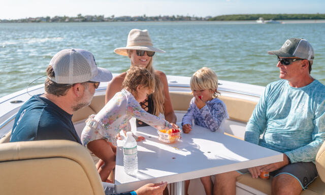 Family of five enjoying food and conversation at the boat's dining table on calm water