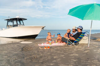 Family with young children relaxing on a sandbar beach with a center console boat nearby and turquoise umbrella for shade