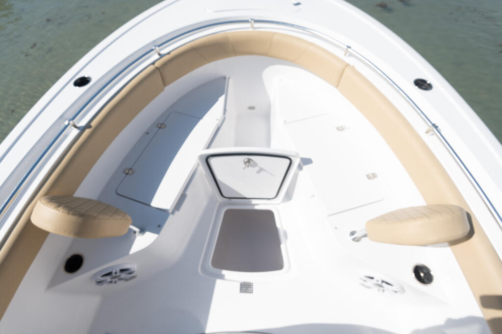 Bow seating area with tan cushioned seats and center storage box with windshield access
