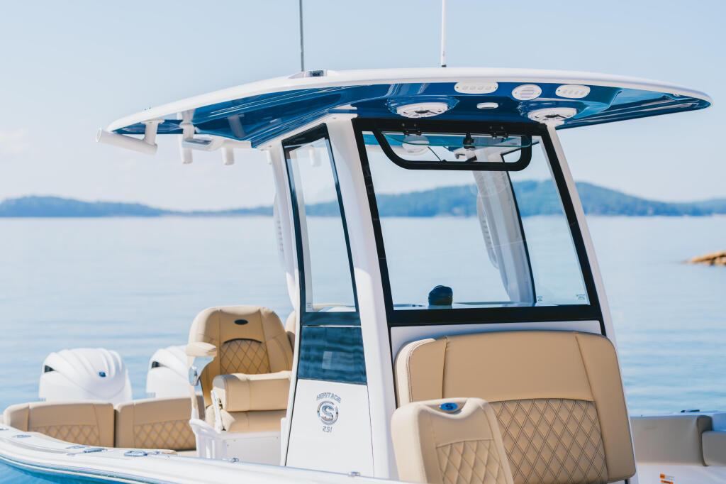 Blue and white center console boat with tan seating and hard-top canopy docked on calm lake
