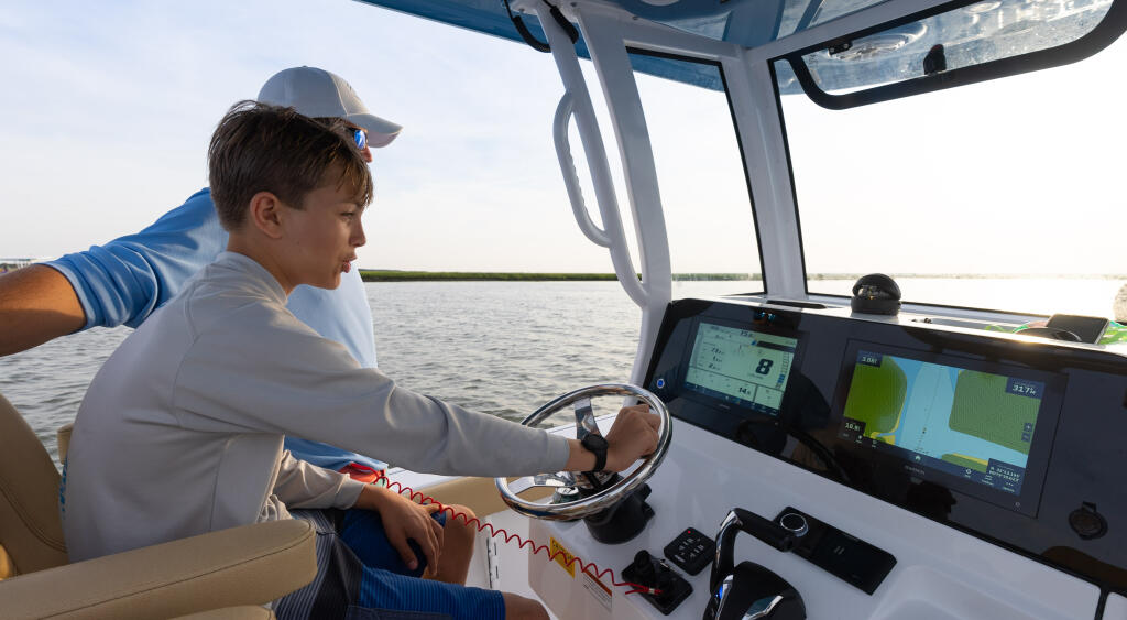 Young boy at the helm steering a boat with digital electronics and navigation displays visible