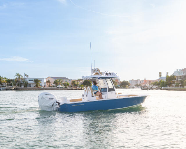 Blue and white center console boat anchored in shallow water near a residential waterfront neighborhood