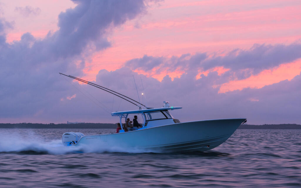 Blue center console boat running through shallow water at sunset with dramatic pink and purple sky