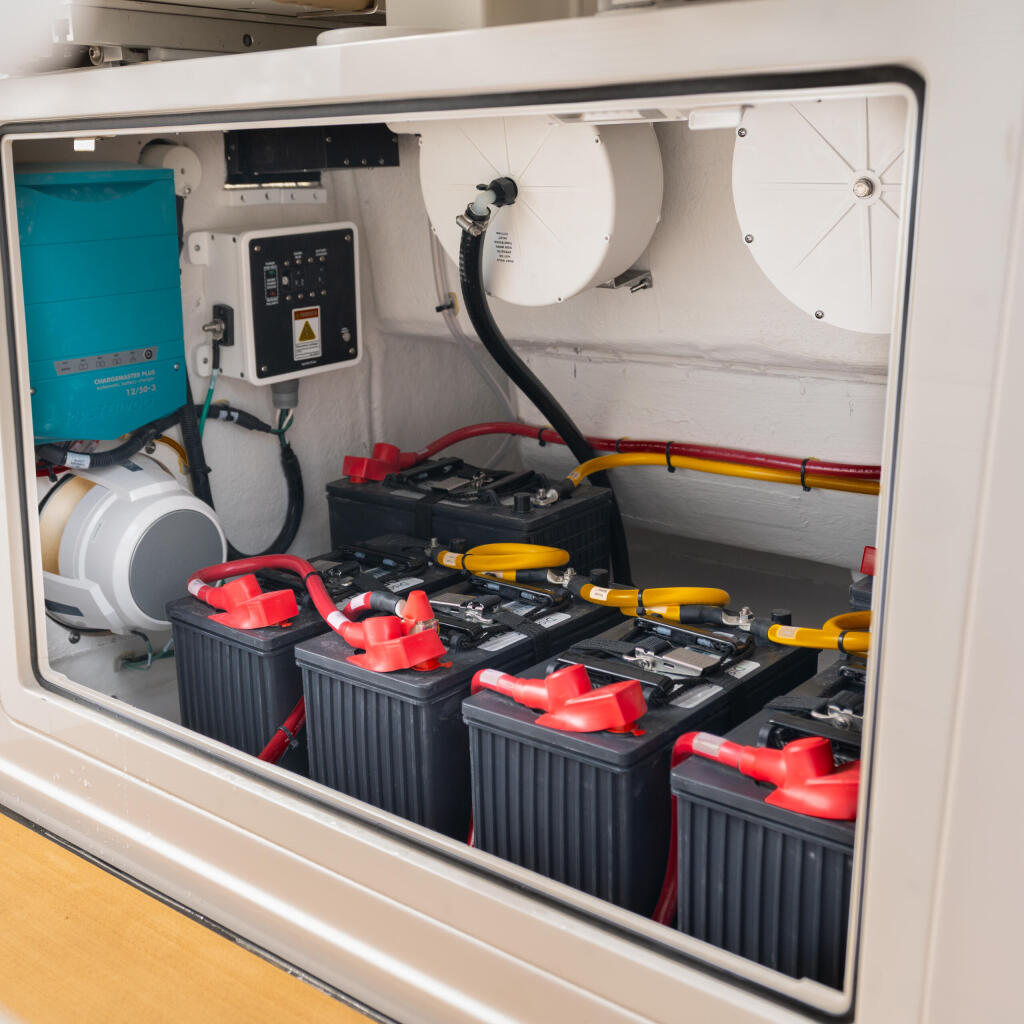 Engine compartment storage showing multiple batteries with red terminals, power inverter, electrical panel, and organized cable management