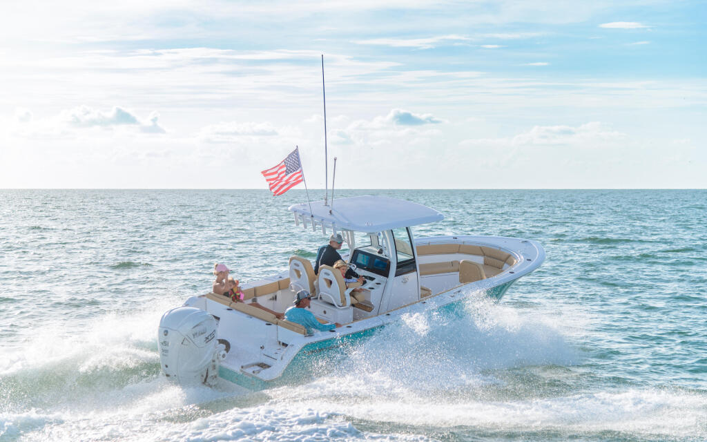 White center console boat with family approaching shallow sandbar waters near beach