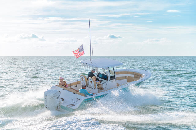 White center console boat with family approaching shallow sandbar waters near beach