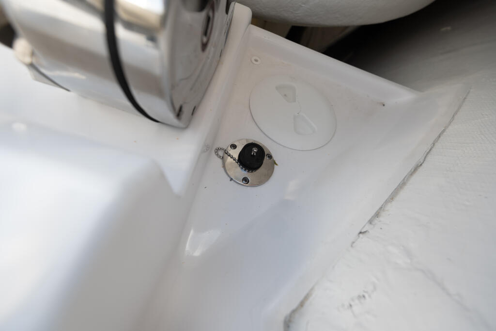 Close-up of boat deck showing anchor locker with black knob control and freshwater washdown fitting