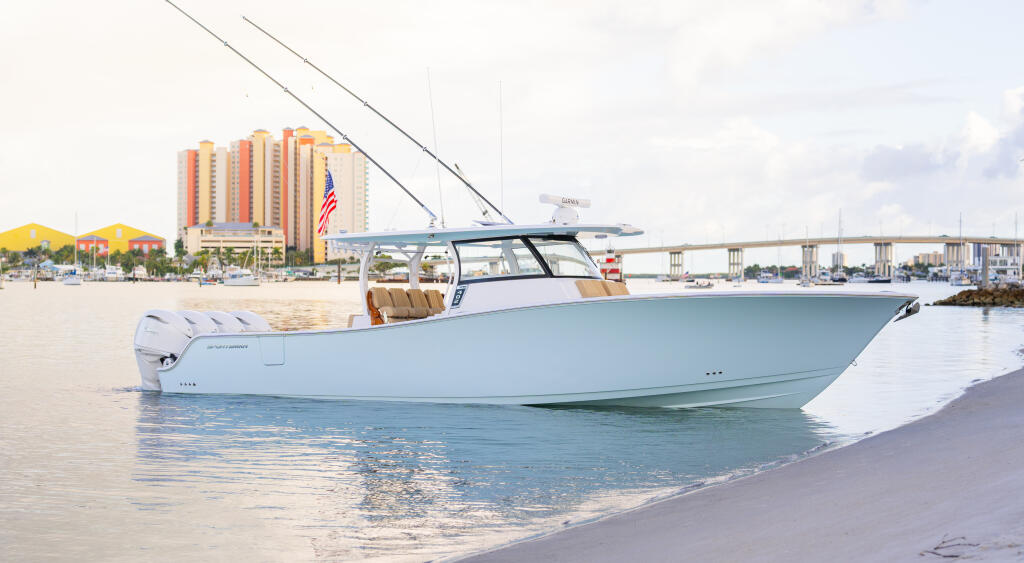 Light blue center console boat beached on sand with a hard-top canopy, near a coastal resort and bridge