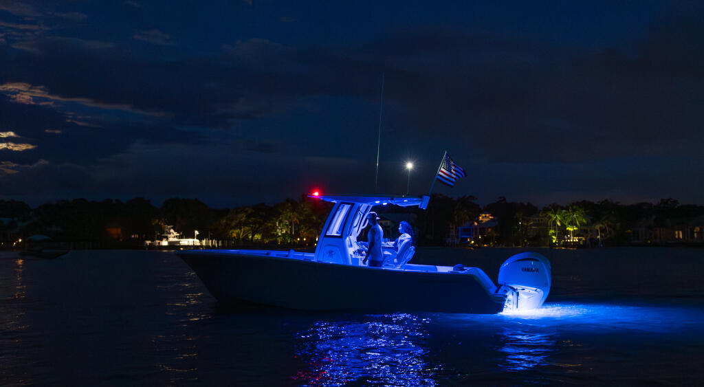 Center console boat illuminated by blue lighting at twilight with antenna and flag visible in calm waterway