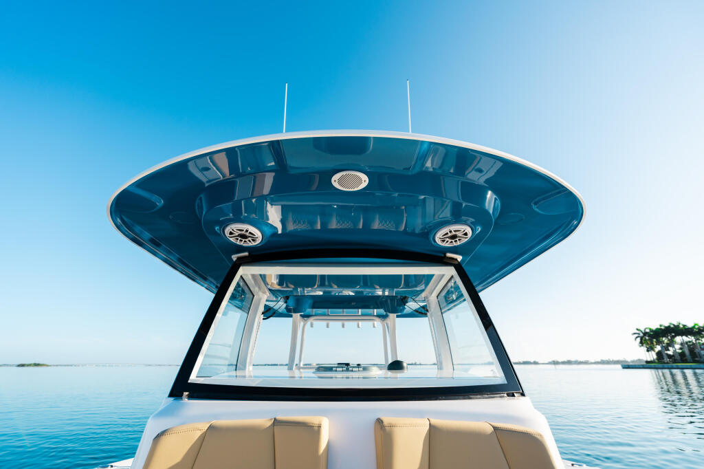 Boat's hard-top cabin with blue cushioned seating and panoramic windshield overlooking calm water