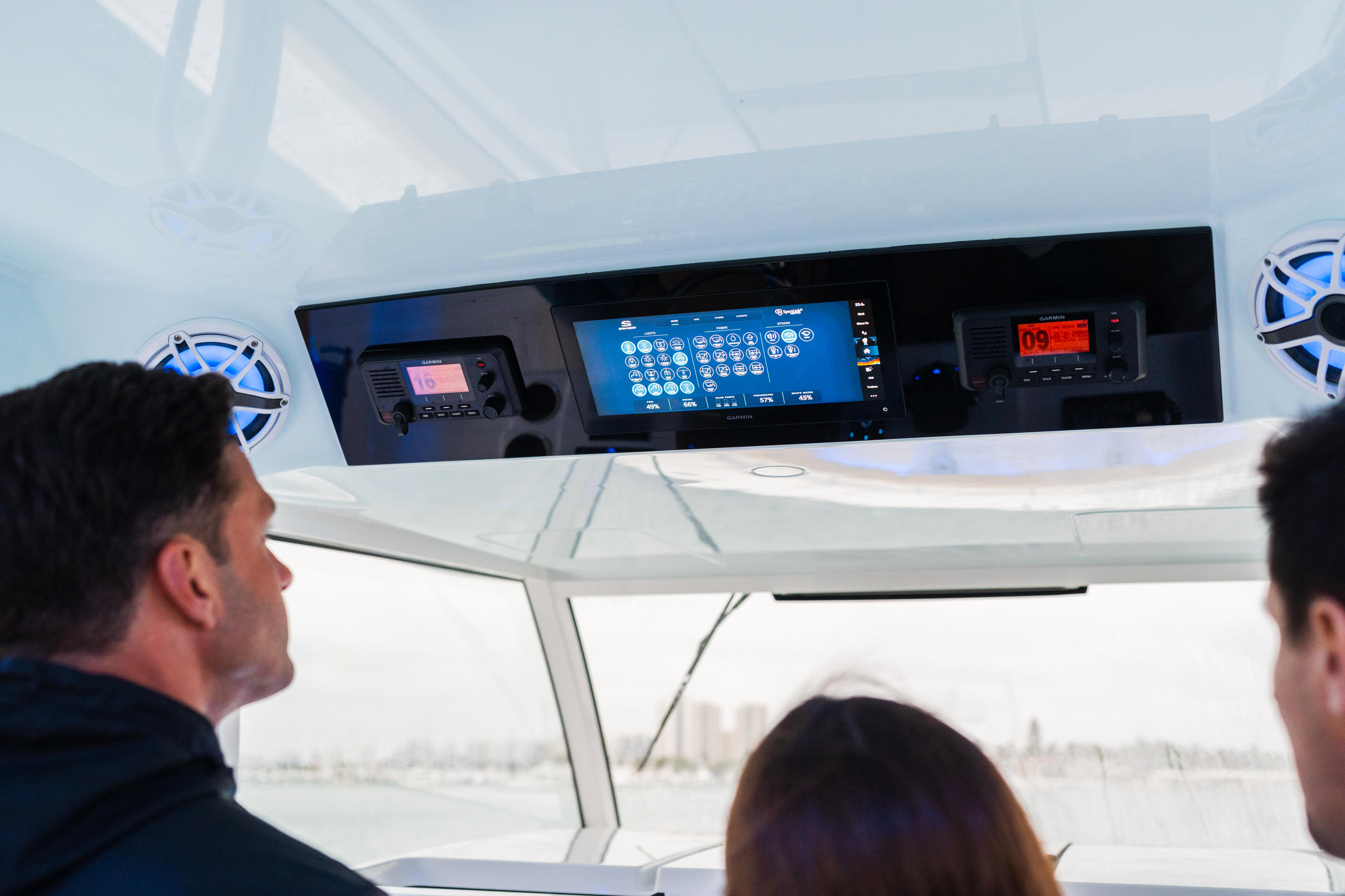Helm station with GPS chartplotter and marine electronics visible through hard-top windshield with passengers aboard