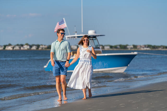 Couple jogging along the beach with an American flag and blue sport fishing boat anchored in shallow water behind them