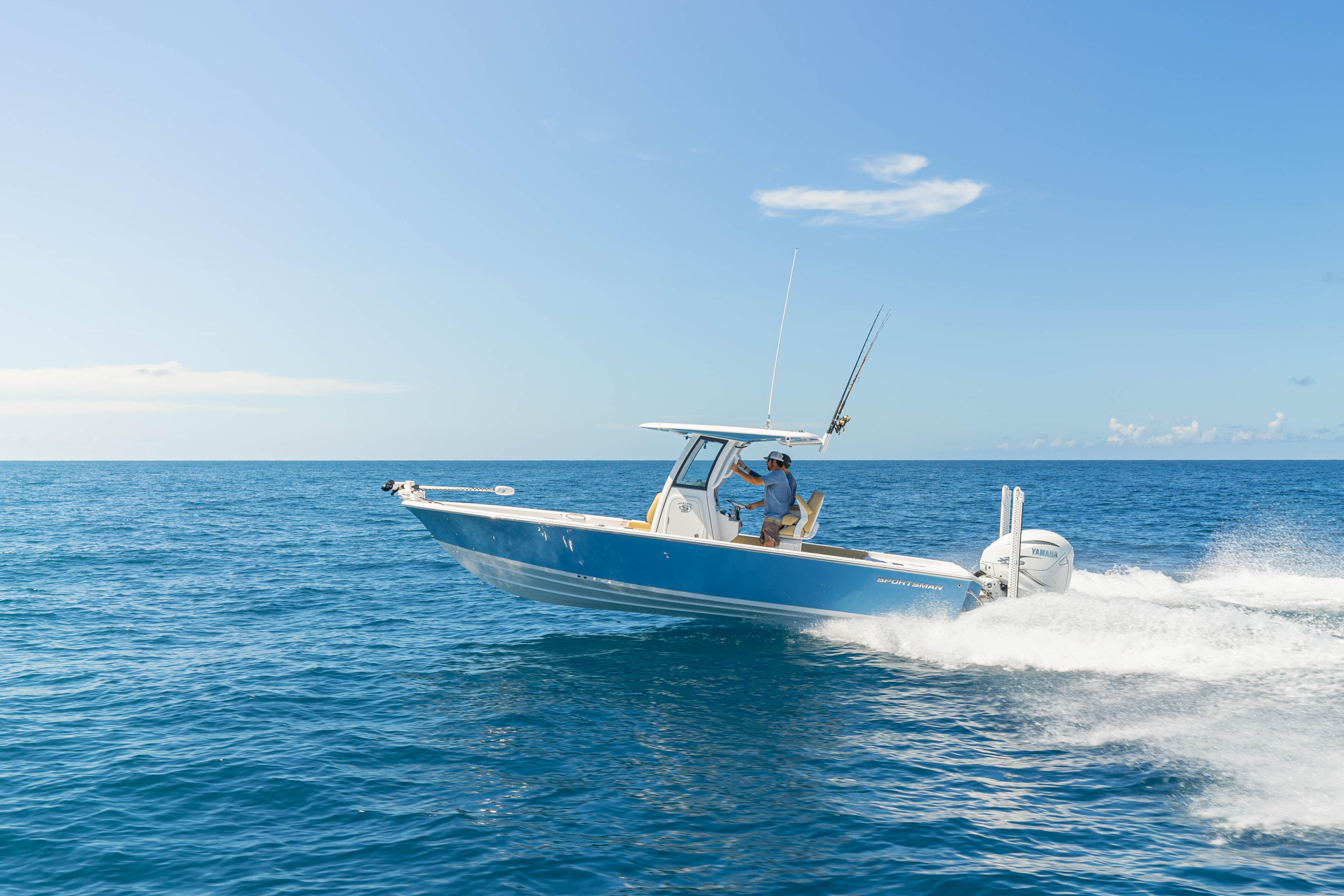 Blue and white fishing boat navigating through shallow coastal waves with fishing rods mounted on the helm