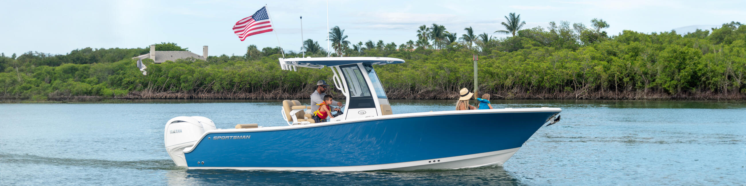 Blue and white center console boat anchored in shallow water with passengers and an American flag, mangroves visible in background