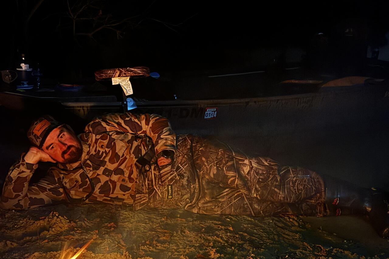 Person relaxing by a campfire on a beach at night with a boat nearby