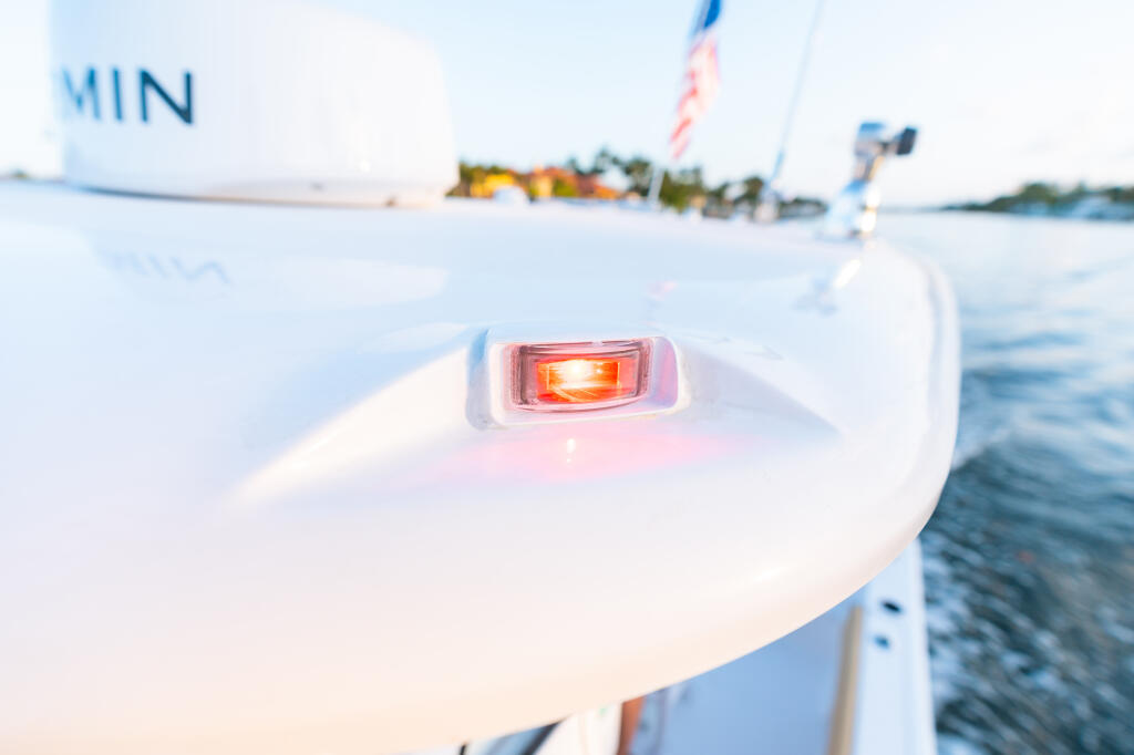 Illuminated red navigation light mounted on white boat hull gunwale with sailboats in background