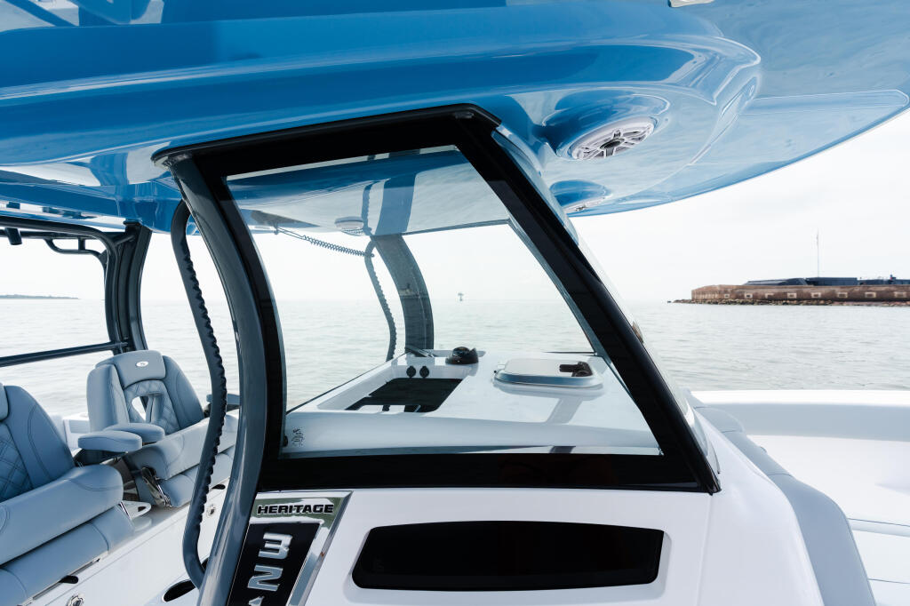 Open windshield view from helm of blue and white center console boat with calm water and marina in background