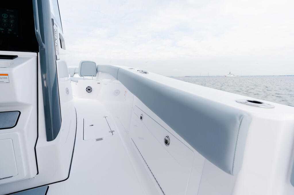 Clean white boat deck with gray cushioned seating and railing, extending toward calm open water