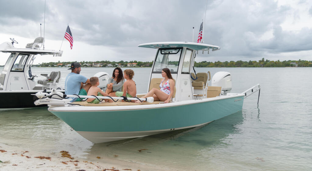 Family relaxing together on a turquoise and white center console boat anchored in shallow water near a sandy beach