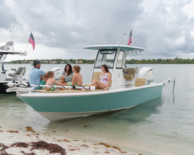 Family relaxing together on a turquoise and white center console boat anchored in shallow water near a sandy beach