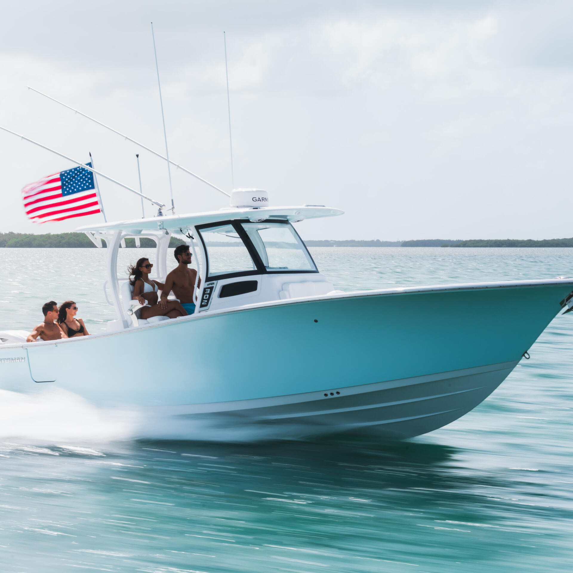Turquoise and white center console boat running through shallow water with four people aboard and American flag flying