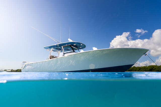 Blue and white sport fishing boat anchored in shallow turquoise water with clear sky