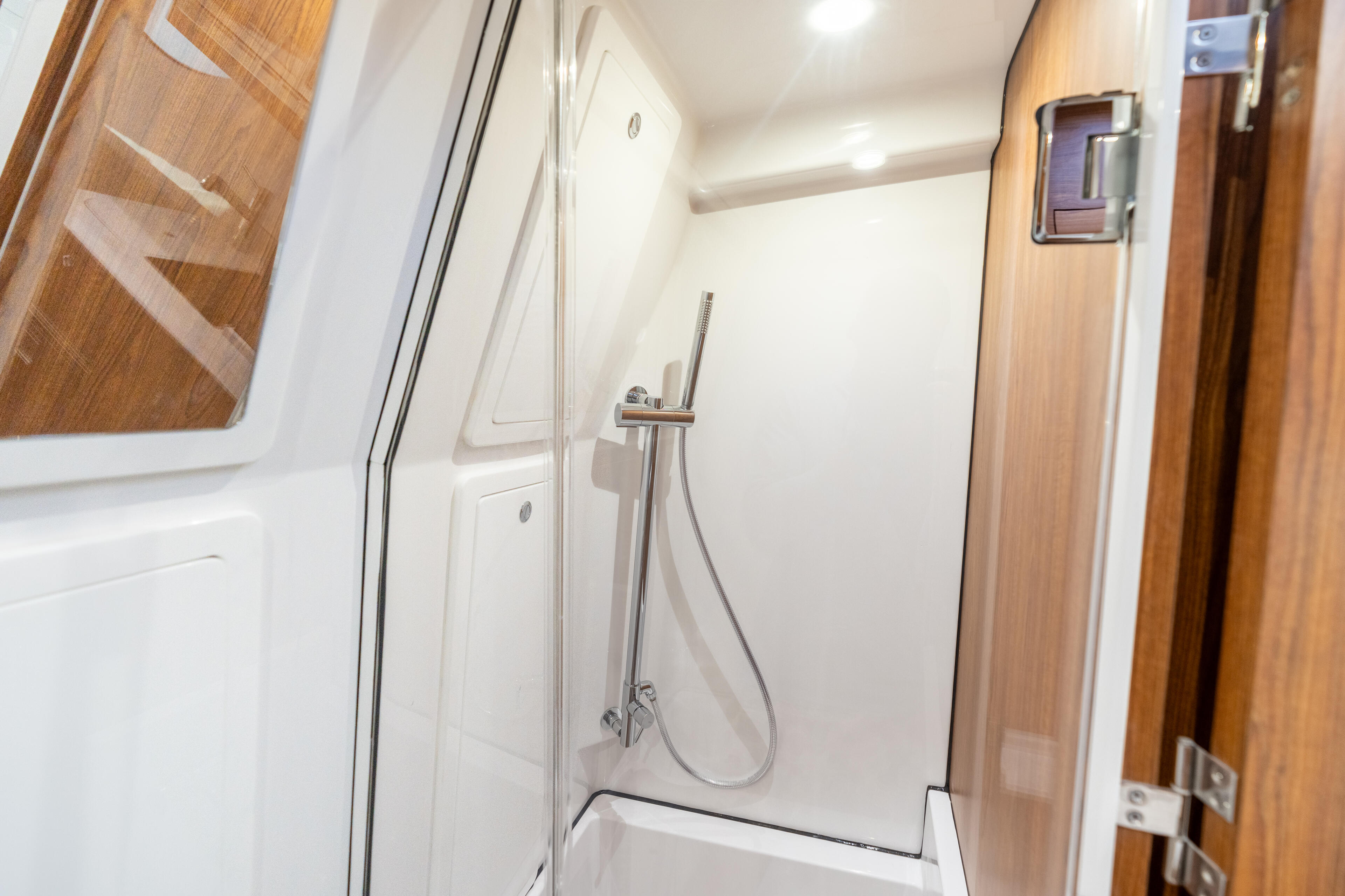 Modern enclosed shower with glass door and chrome fixtures inside a boat cabin