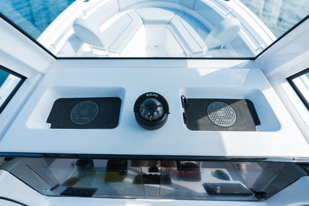 Helm console with dual speakers and Ritchie compass mounted on white hardtop with glass windshield