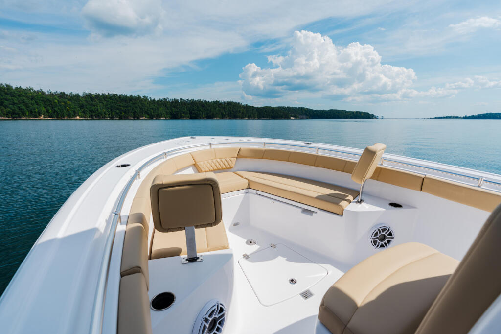 Bow seating area of a white powerboat with tan cushions on calm lake waters surrounded by forested shoreline