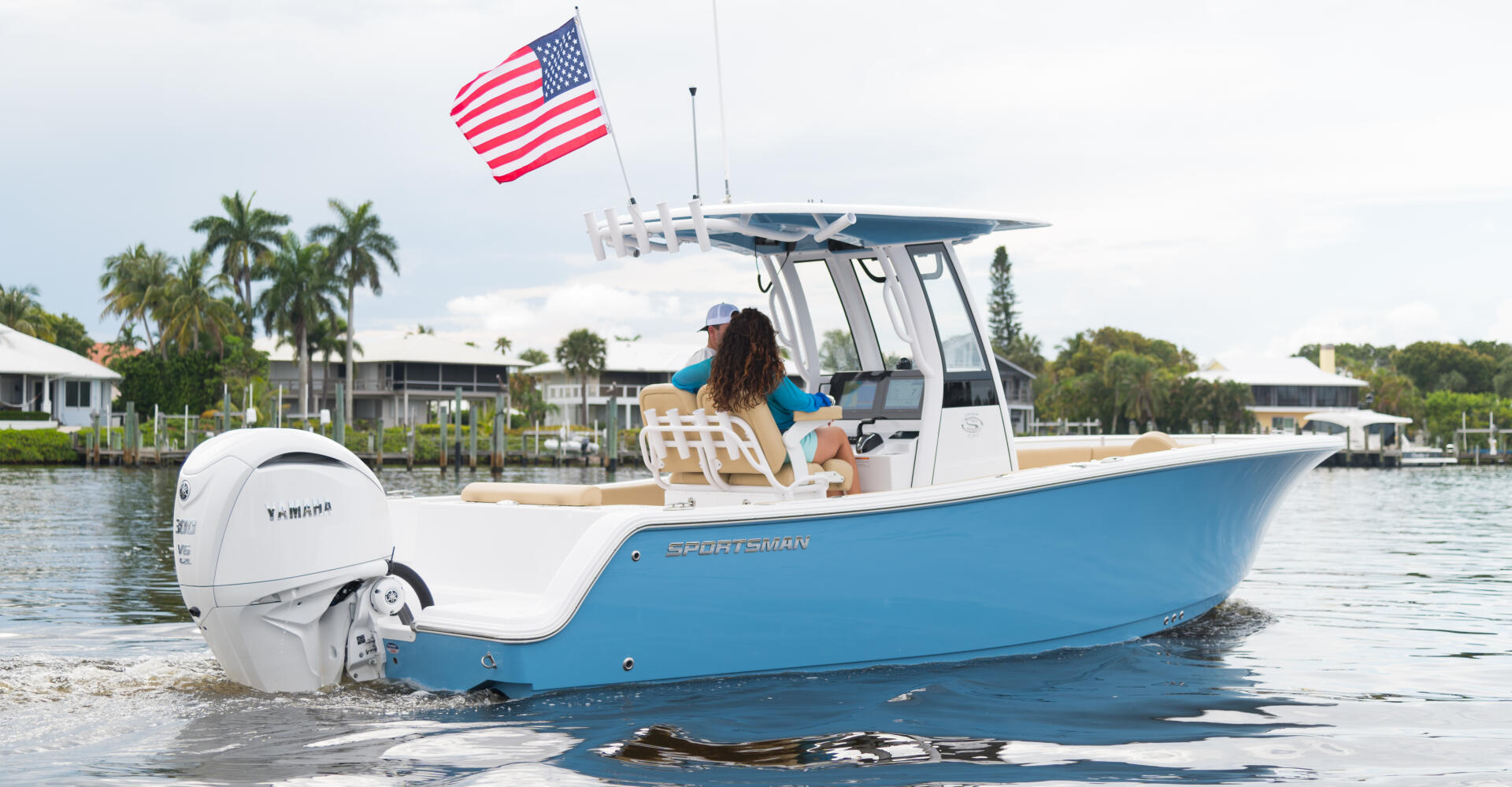 Blue and white center console boat anchored in shallow sandbar waters with American flag and hard-top canopy