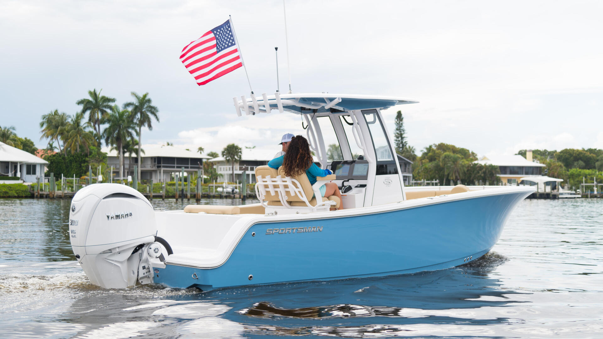 Blue and white center console boat anchored in shallow sandbar waters with American flag and hard-top canopy