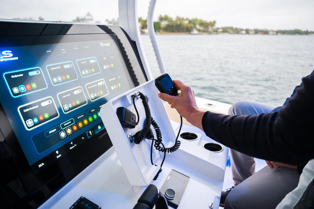 Captain holding handheld radio while operating boat's advanced touchscreen helm in open water